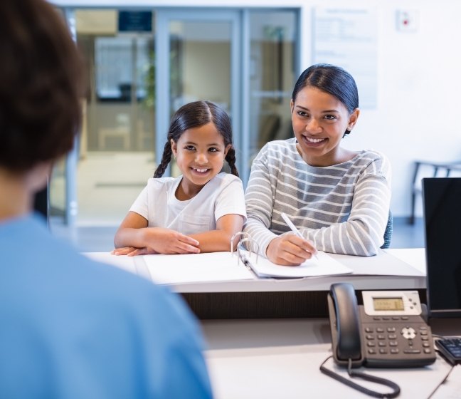 Mother and child at dental office reception desk discussing the cost of dental emergencies