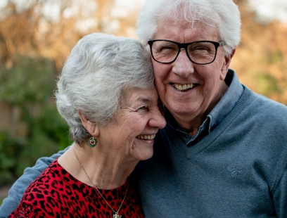 Senior man and woman smiling and holding each other outdoors
